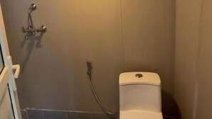 A bathroom with a toilet, shower, and a small window.