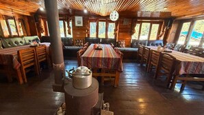 A rustic wooden interior with a central dining table, benches, and a wood stove.