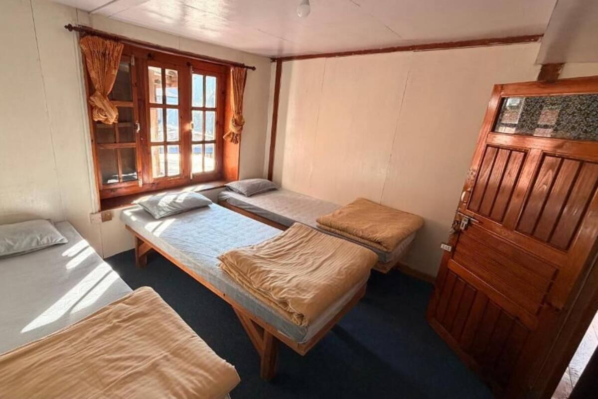 A room with three beds, a wooden wardrobe, and a window with curtains.