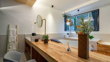 Un baño moderno con tocador de madera, espejo redondo, bañera y ventana con cortinas.