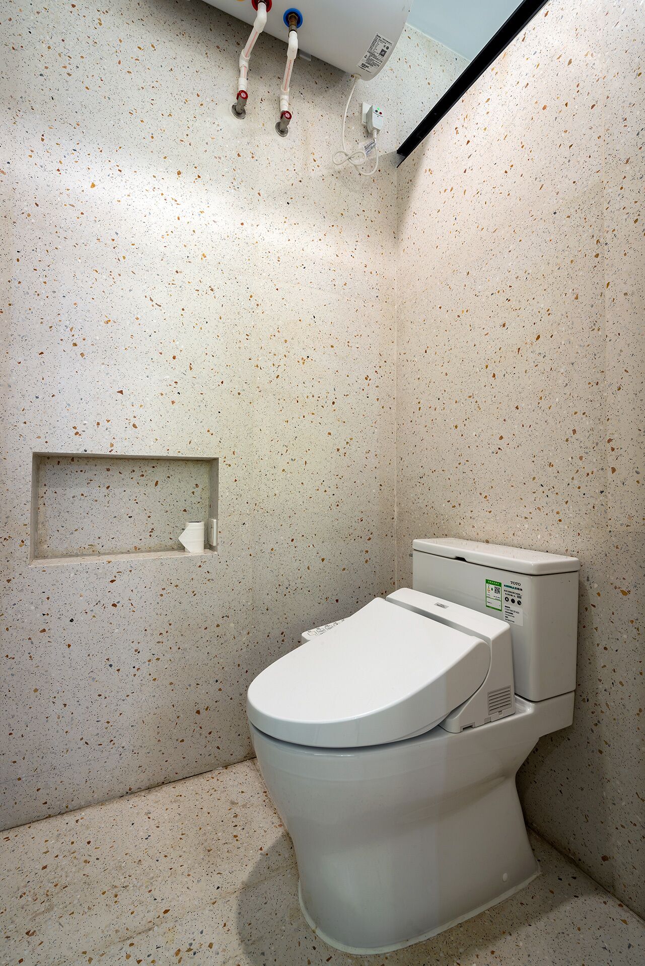 A compact bathroom with a white toilet, a small shelf, and a wall-mounted water heater.