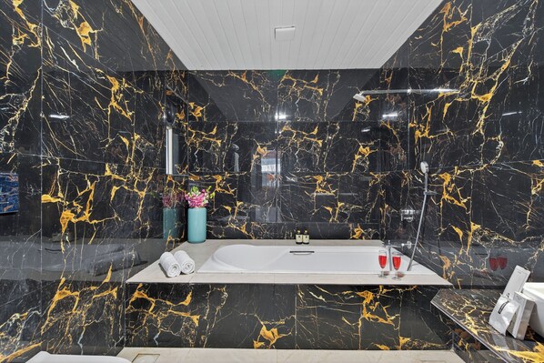 A modern bathroom with a black and gold marble design, a large bathtub, and a glass-enclosed shower. - Alaya Stays Lavender Hills 3BHK Villa (Lonavala)