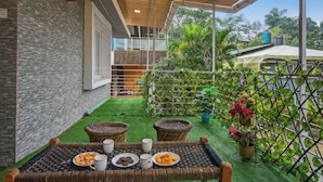 A patio with a table set for two, surrounded by greenery and a view of the building's interior. - Alaya Stays Lavender Hills 3BHK Villa (Lonavala)