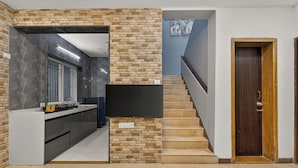 A modern kitchen with a stone accent wall, a built-in TV, and a staircase leading to a second floor. - Alaya Stays Lavender Hills 3BHK Villa (Lonavala)