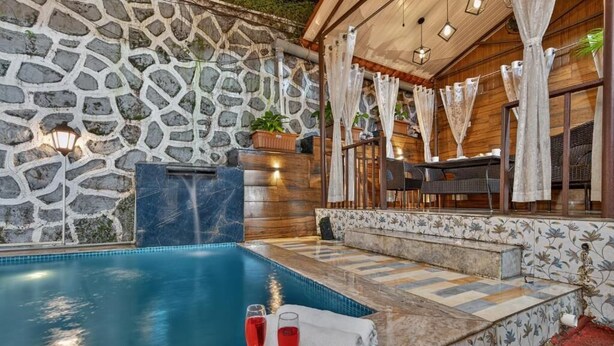 A stone wall, a pool, and a seating area with a table and chairs. - Alaya Stays Lavender Hills 3BHK Villa (Lonavala)
