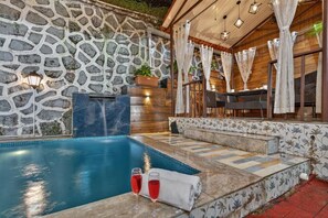 A stone wall, a pool, and a seating area with a table and chairs. - Alaya Stays Lavender Hills 3BHK Villa (Lonavala)