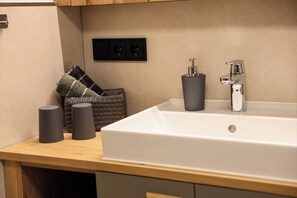 A bathroom with a white bathtub, two cylindrical containers, a towel, and a power outlet on the wall. - Vacation apartment Ertlsteg (Ramsau bei Berchtesgaden)