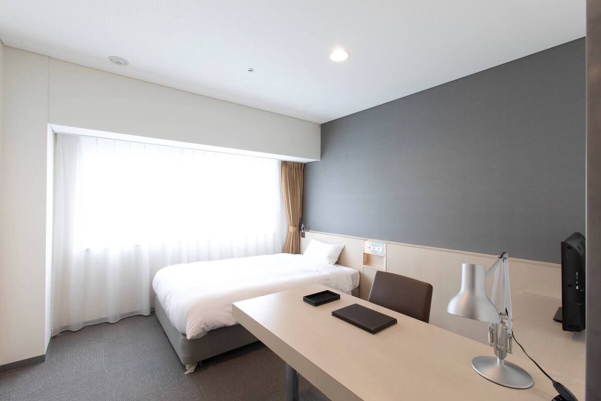 Una habitación de hotel con una cama, un escritorio con lámpara, una silla y un televisor.