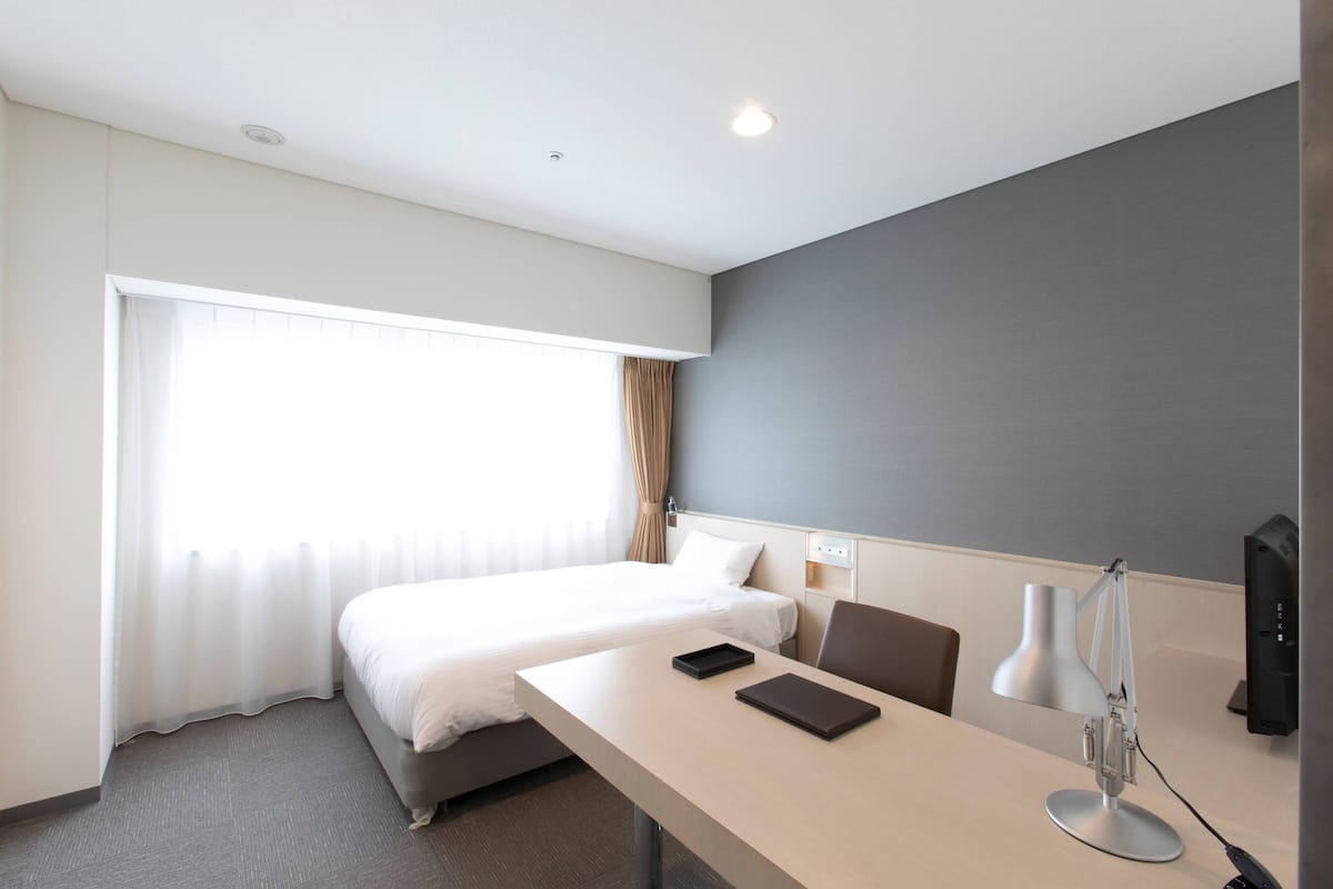 Ein Hotelzimmer mit einem Bett, einem Schreibtisch mit Lampe, einem Sessel und einem Fernseher.