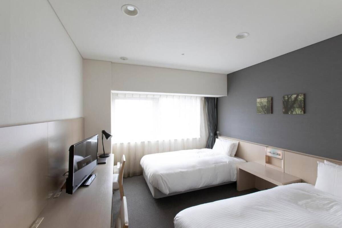 Habitación de hotel con dos camas, televisión, escritorio y ventana con cortinas.