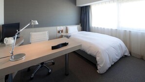 Habitación de hotel con cama, escritorio con lámpara, televisión y ventana con cortinas.