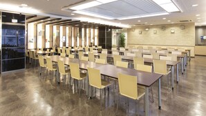 Una amplia sala de conferencias con largas mesas y sillas, un techo alto con iluminación empotrada y una pared de ladrillo con cuadros enmarcados.