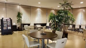 Un salón de conferencias con una mesa redonda, sillas blancas, una planta en maceta y un tablón de anuncios.