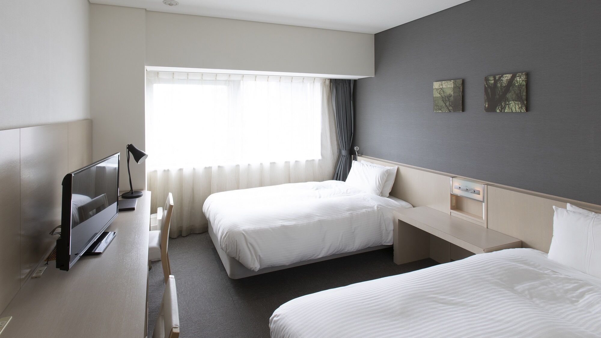 A hotel room with two beds, a desk, a TV, and a window with curtains.
