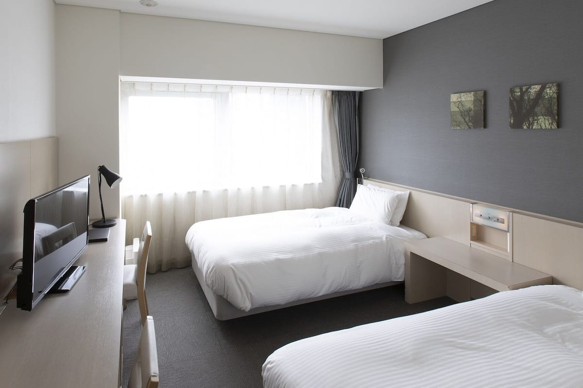 Habitación de hotel con dos camas, un escritorio, un televisor y una ventana con cortinas.
