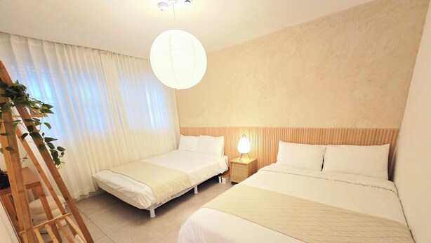 Une chambre d’hôtel avec deux lits, une échelle en bois, une table de chevet avec une lampe et une grande fenêtre avec des rideaux.