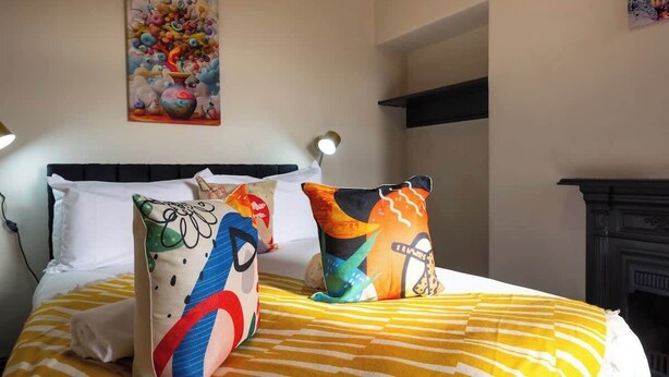 Een bed met kleurrijke kussens en een schilderij aan de muur.