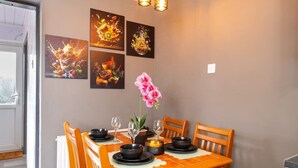 Een eetgedeelte met een tafel gedekt voor vier personen, omringd door stoelen, met kunst aan de muur en een potplant.