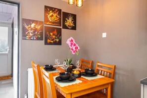 Un coin repas avec une table dressée pour quatre personnes, entourée de chaises, et agrémenté d’œuvres d’art au mur et d’une plante en pot.