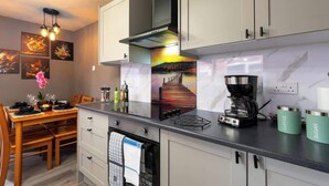 Een moderne keuken met een inbouwfornuis, koffiezetapparaat en een eethoek met een tafel en stoelen.