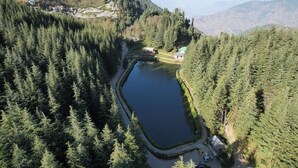 Un lago rodeado de un bosque frondoso, algunas edificaciones y una carretera.