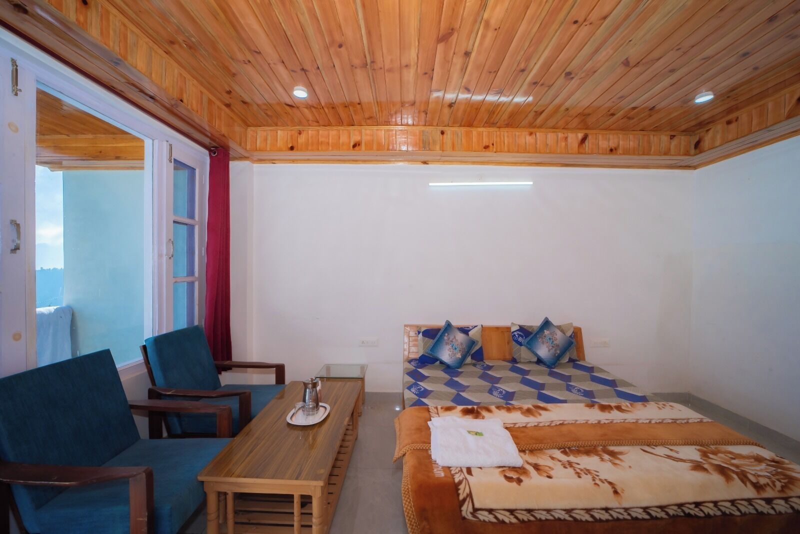 Une pièce avec un plafond en bois, un lit avec une literie à motifs, une table avec des chaises et une fenêtre donnant sur un paysage agréable.
