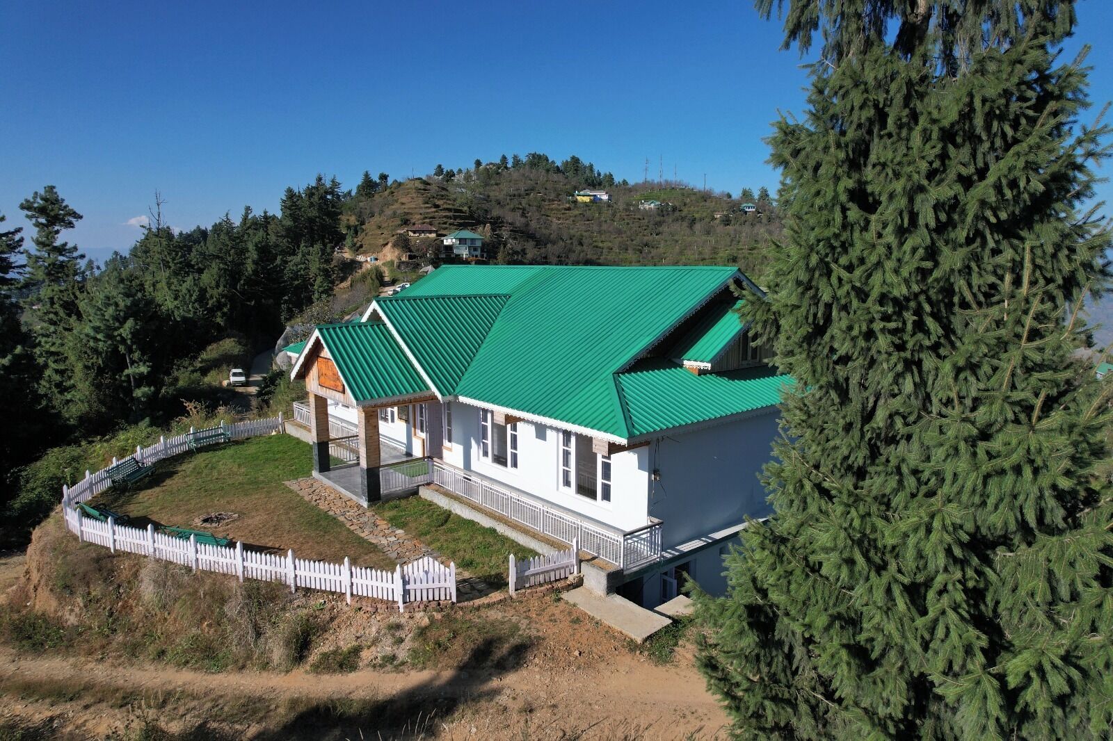 Una casa con techo verde, paredes blancas y valla blanca.