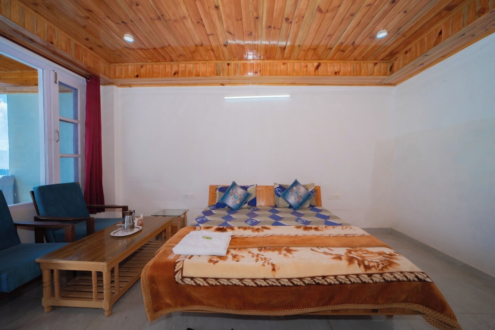 A room with a bed, a wooden table, a chair, and a window with curtains.