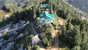 Un refugio de montaña con techo verde, rodeado de un bosque frondoso y un camino de tierra.