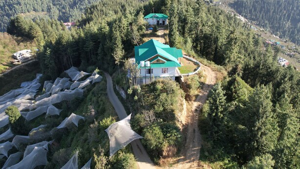 Un paisaje montañoso con dos casas de techos verdes, rodeadas por un bosque denso.