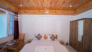 Un dormitorio con techo de madera, una cama con dos almohadas, un armario de madera y una ventana con cortinas.
