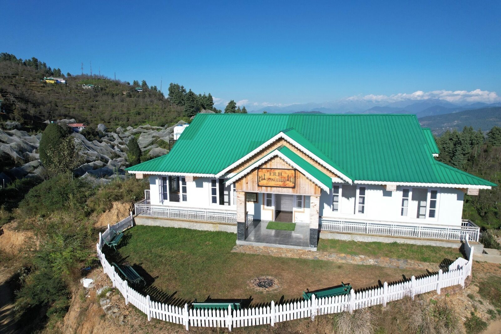 A two-story building with a green roof, a white picket fence, and a signboard.