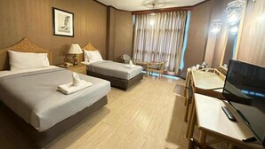 A hotel room with two beds, a desk with a chair, a television, and a window with curtains. - Lertthanee Hotel (Suphan Buri)