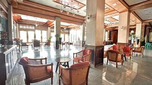 A spacious lobby with high ceilings, wooden paneling, and a polished marble floor. There are wicker chairs and tables arranged for seating. - Lertthanee Hotel (Suphan Buri)