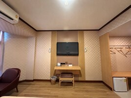 A hotel room with a wooden desk, a television, a chair, a small table, and a mini-fridge.