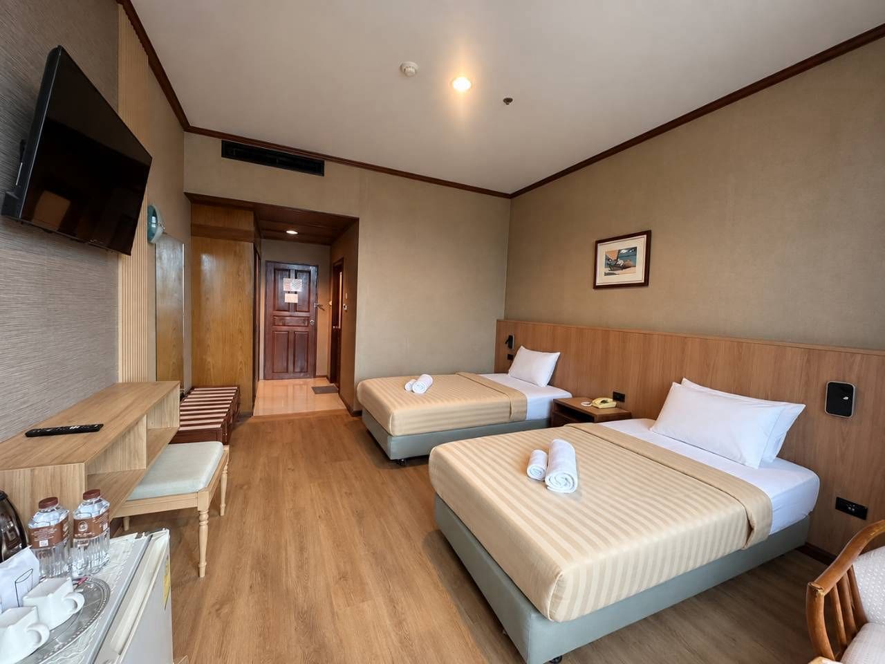A hotel room with two beds, a desk with a chair, a TV mounted on the wall, and a door leading to a hallway.