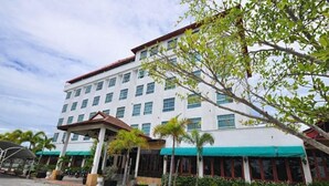 A multi-story hotel with a white facade, multiple windows, and a covered outdoor area with palm trees. - Lertthanee Hotel (Suphan Buri)