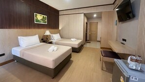 A hotel room with two beds, a desk, a TV, and a door leading to a hallway. - Lertthanee Hotel (Suphan Buri)