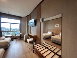 A hotel room with a bed, a desk, a chair, a TV, and a large window with a city view.