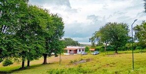 Landelijk landschap met een klein gebouw, mogelijk een huis of gastenverblijf, omringd door bomen en open grasvelden.