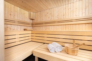 Una sauna con bancos de madera y un banco con toallas y un cubo de madera.