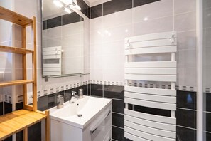 A modern bathroom with a white sink, black and white tiles, a wooden shelf, and a towel rack. - Chalet in Paradiski With Spa & Stunning Views (Peisey-Nancroix)