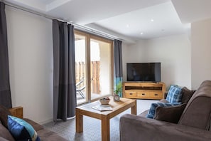 A living room with a sofa, a coffee table, a TV, and a sliding glass door leading to an outdoor area. - Chalet in Paradiski With Spa & Stunning Views (Peisey-Nancroix)