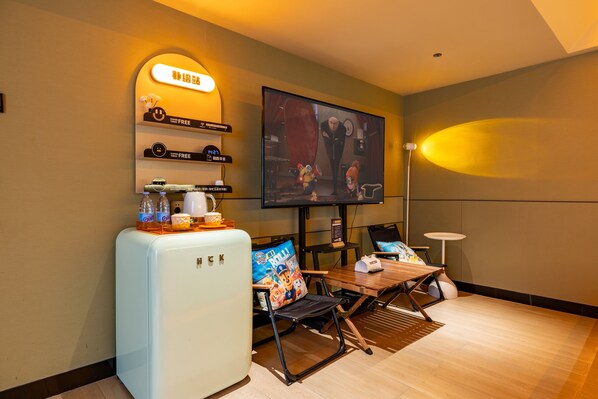 A room with a flat-screen TV mounted on the wall, a small refrigerator, a wooden table with chairs, and a small side table with a lamp. - Super-Times Hotel (Guangzhou)