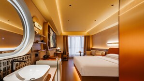 Una habitación de hotel moderna con una bañera ovalada grande, una cama con sábanas blancas, un espejo grande y un televisor en la pared.