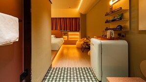 Habitación de hotel pequeña con cama, zona de estar, kitchenette y baño.