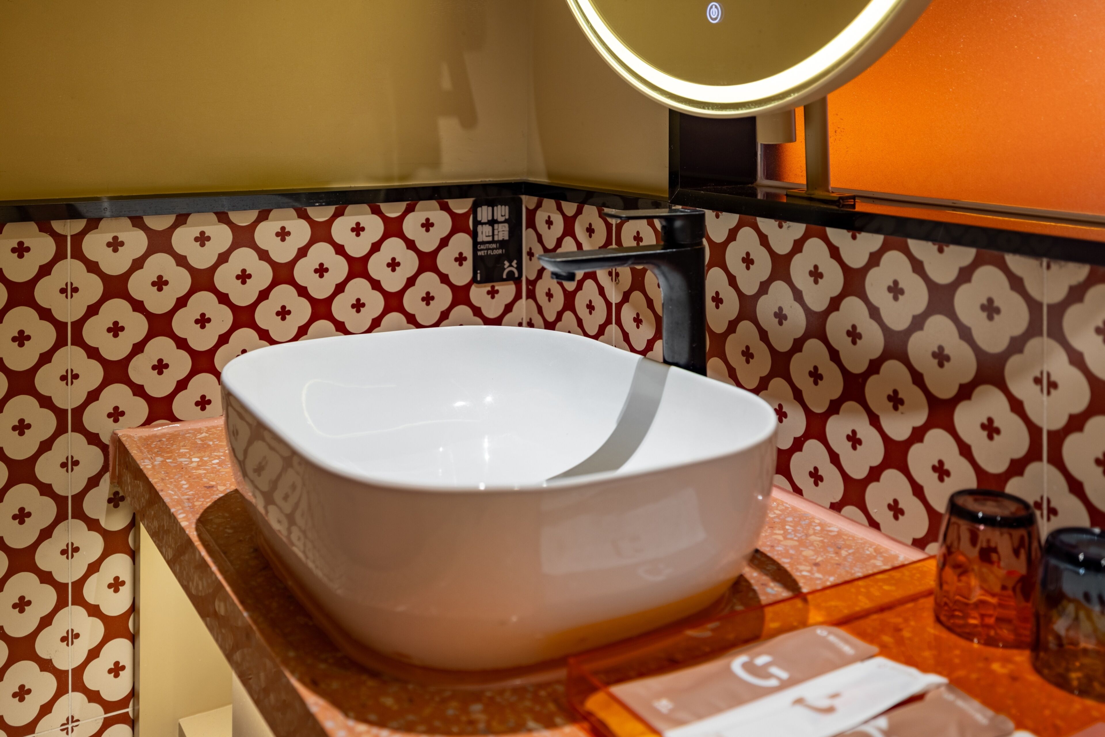 A bathroom with a white vessel sink, a mirror, and patterned walls.