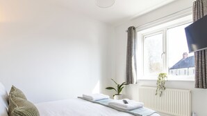A bedroom with a bed, a window, a radiator, and a plant. - One Bed Apartment in Wellington (Telford and Wrekin)