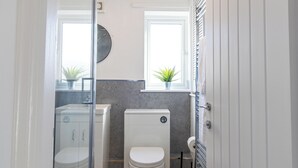 A compact bathroom with a toilet, a sink, and a shower area. There are two potted plants on the windowsill. - One Bed Apartment in Wellington (Telford and Wrekin)