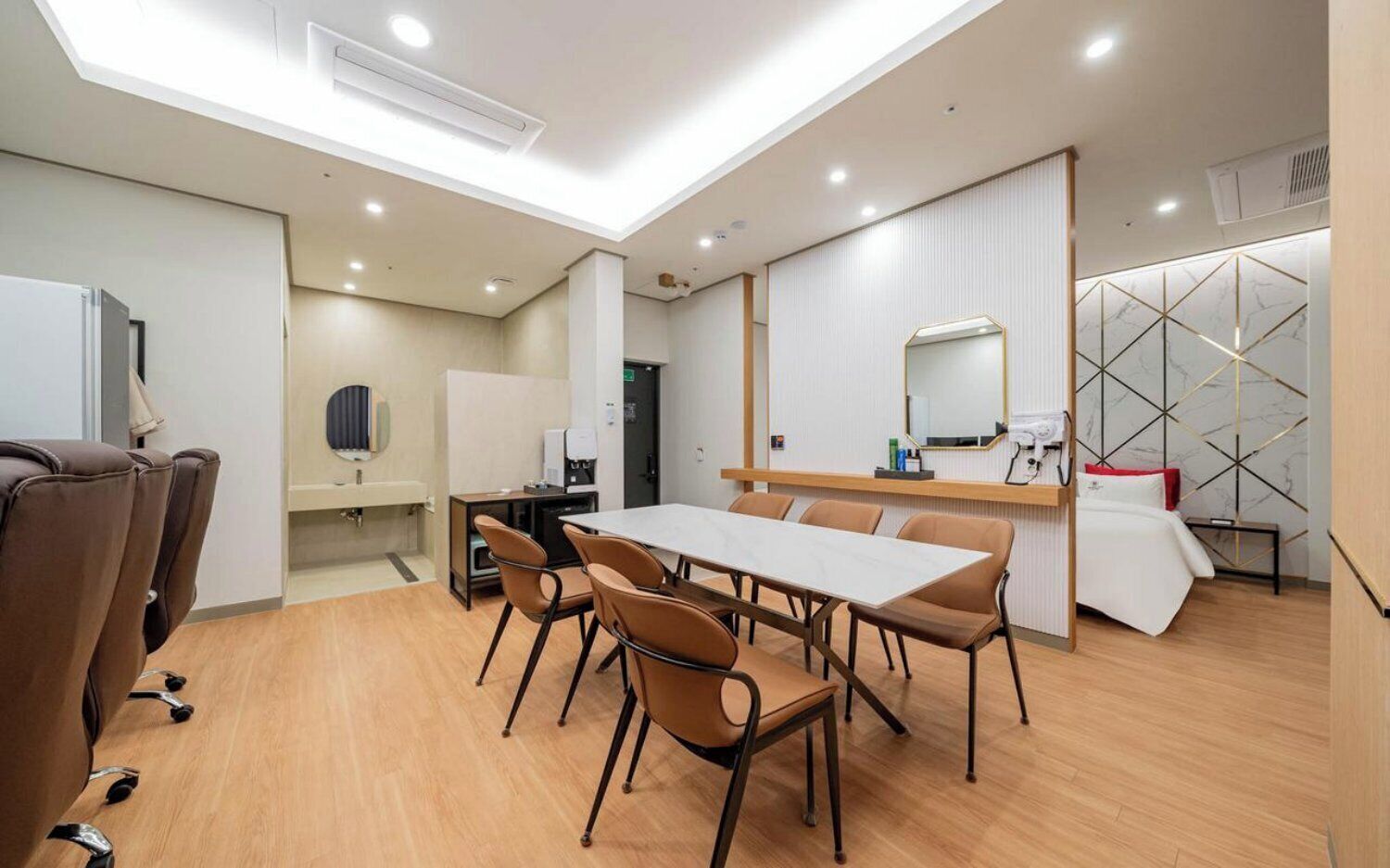 A modern hotel room with a dining area, a small kitchenette, and a bed with a decorative wall.